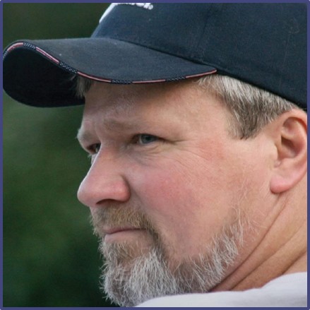 Side profile headshot of Allan Evald wearing a blue baseball cap