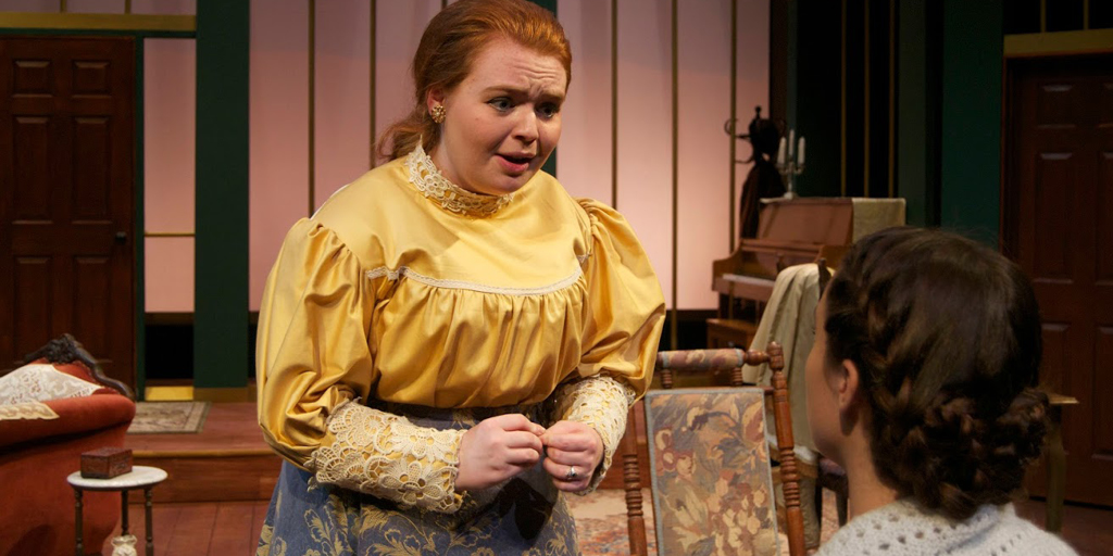 Theatre image of a red headed woman in yellow shirt talking to a man