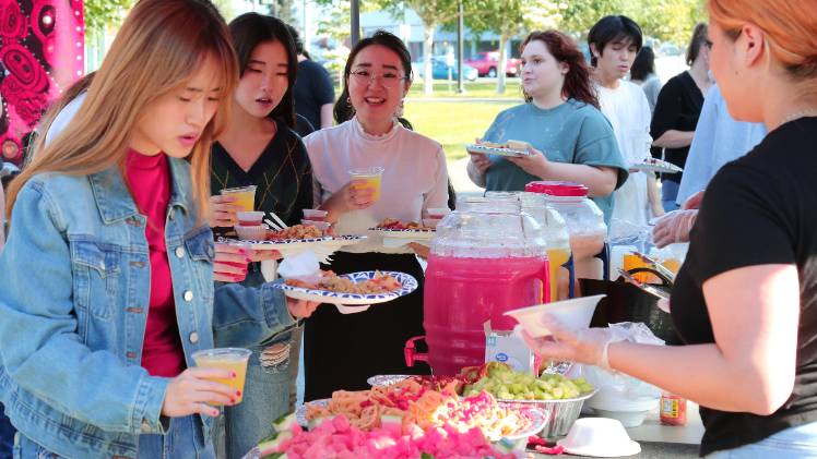 Students at a campus event in line collecting food and drinks. The food and drinks on the table are colorful and bright including agua fresca drinks and fresh fruits.