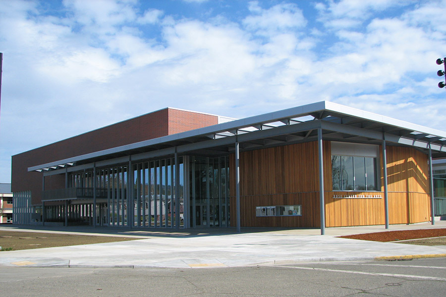 Rose Center for the Arts Rose Center for the Arts, a modern building with a mix of wooden and glass facades, featuring large windows and a flat roof against a cloudy sky.