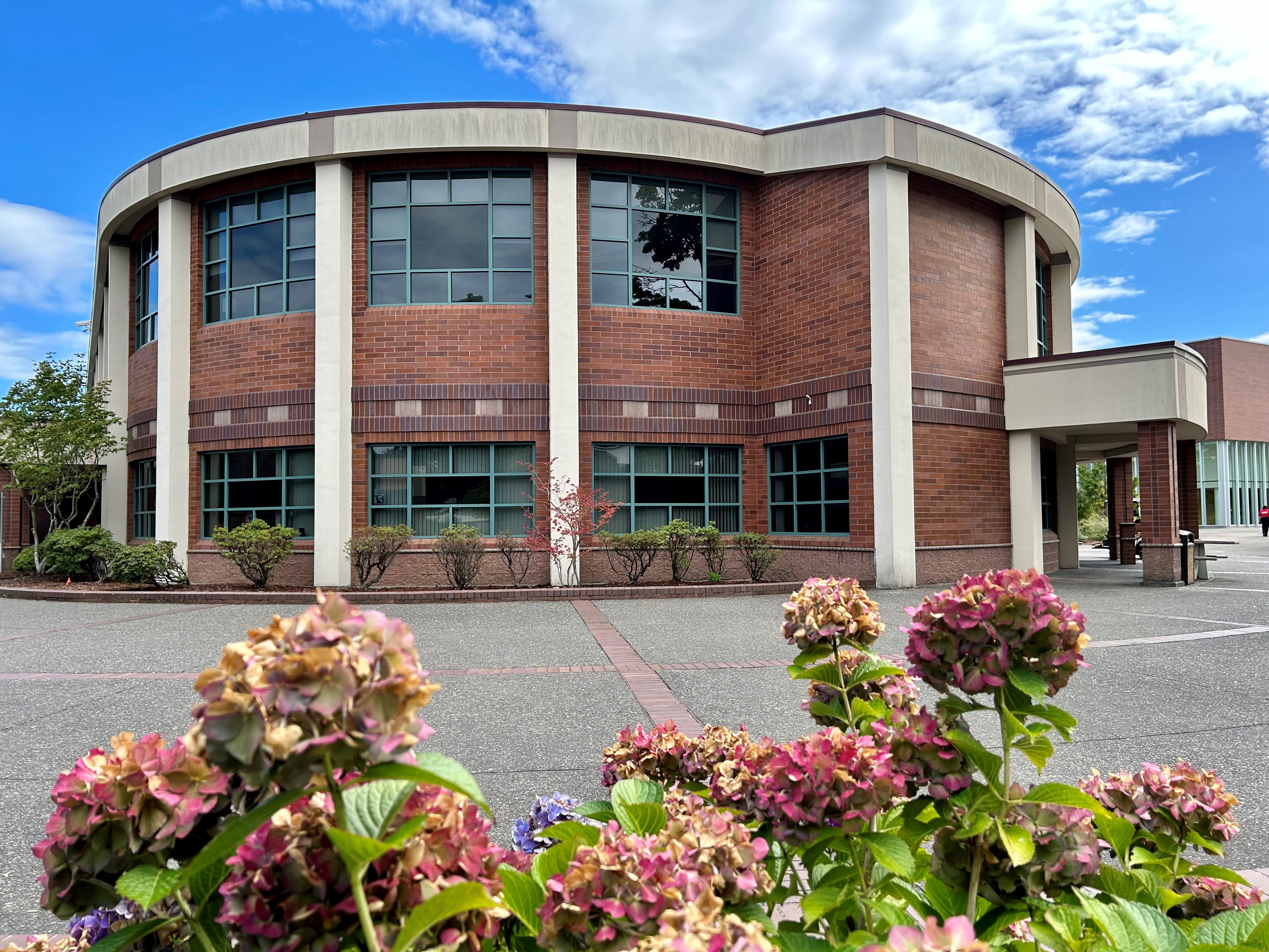 Student Center Student Center, a modern brick building with large windows, surrounded by blooming flowers and a clear blue sky above.